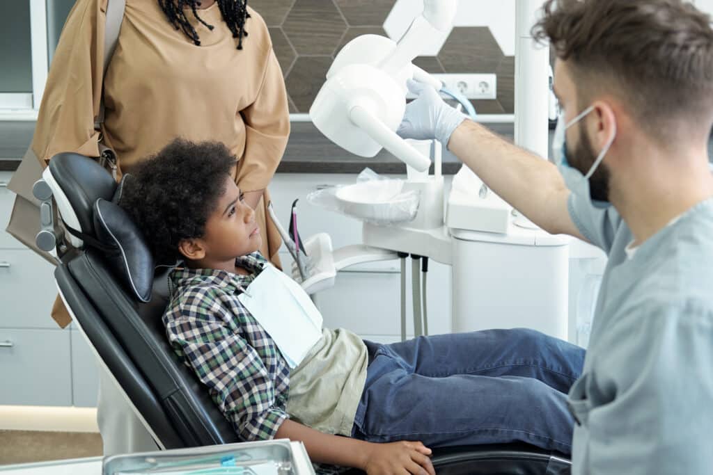 Little African boy looking at medical lamp while sitting in armchair in dental office